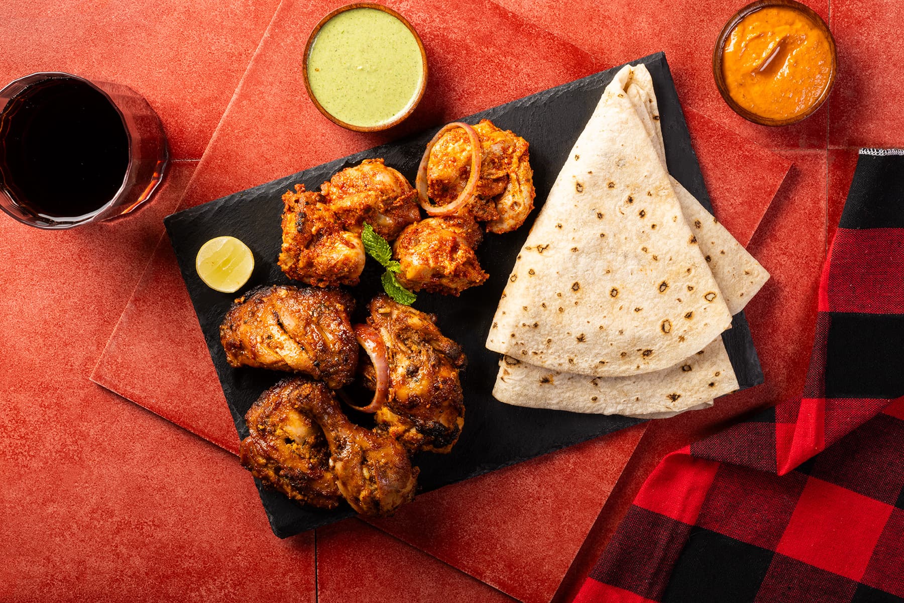 Chicken tikka on a slate board with rumali roti and chutneys